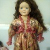 A doll with long dark brown hair wearing a light brown floral dress