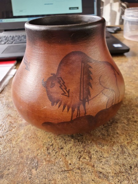 A brown and black ceramic pot with an image of a bison with a lightning bolt.