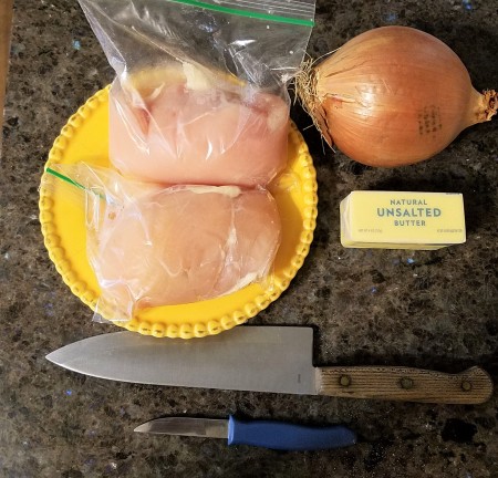 Chicken breasts in plastic bags next to an onion and butter and knives.