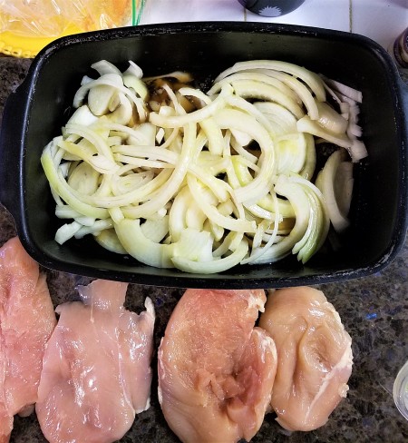 Four chicken breasts next to the pan with the sliced onions.