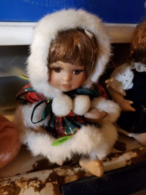 Little girl doll wearing a red and green plaid, white fur trimmed outfit