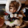 Little girl doll wearing a red and green plaid, white fur trimmed outfit