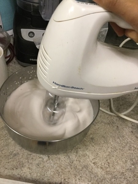 Using a hand mixer to whip the meringue mixture.