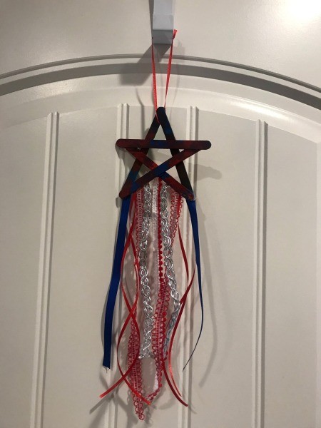 4th of July Craft Stick Star with Streamers - star decoration hanging by ribbon to over the door hanger against a white door