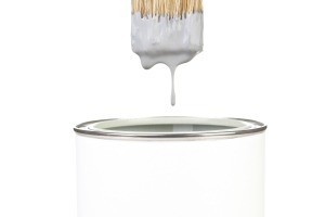 A can of white paint with a dripping paintbrush.