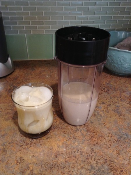 A glass of oat milk next to the blender container.