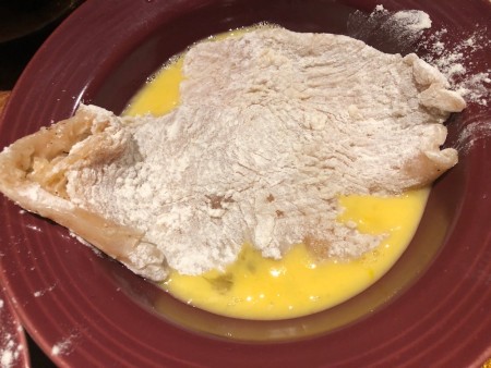 Breaded chicken cutlets being dredged in egg.