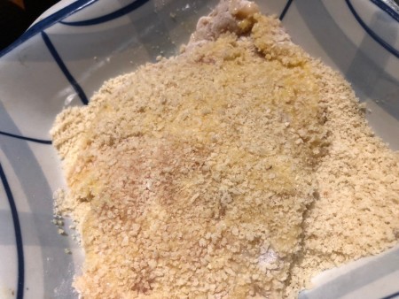 Breaded chicken cutlets being dredged in breadcrumbs.