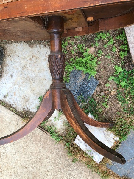 A wooden table with a single leg that has three feet.