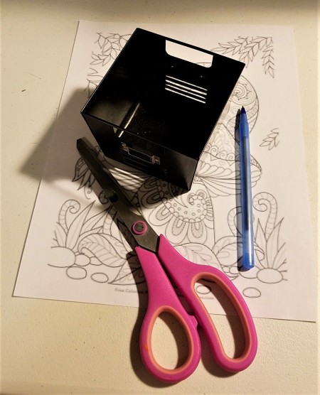 A metal box with scissors, pen and scrap paper.