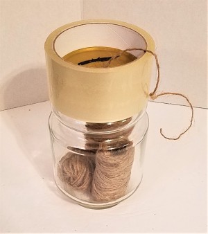 A roll of tape on top of a recycled glass jar containing a roll of twine.