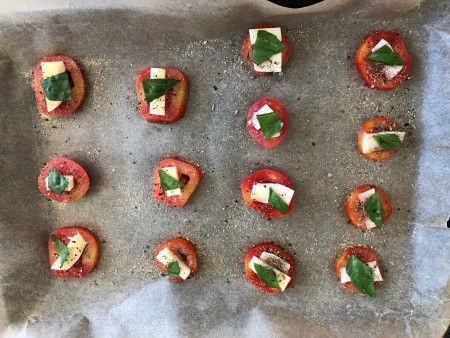 Halved tomatoes, mozzarella and basil, ready for baking.
