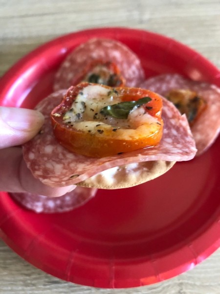 A baked tomato served on salami topped cracker.