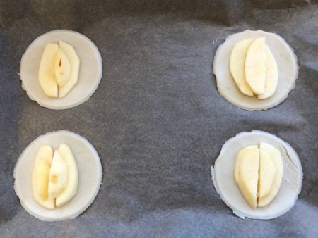 Round pie crusts topped with apple, before baking.