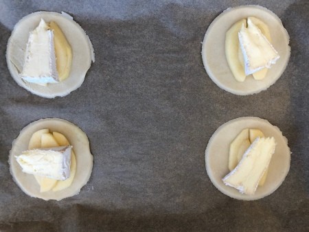 Round pie crusts topped with apple and brie, before baking.