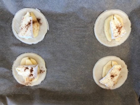 Round pie crusts topped with apple and brie, before baking.
