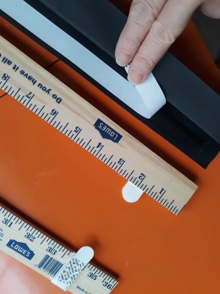 Attaching an accordion shade to a yardstick.
