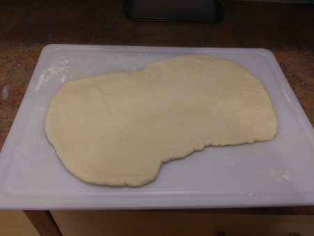 Flattened bread dough on a cutting board.