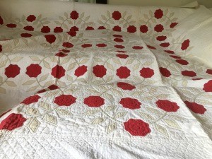 An old quilt with appliqué of red flowers and diamond shaped leaves on white background.