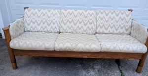A wood frame sofa with light colored cushions.