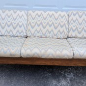 A wood frame sofa with light colored cushions.