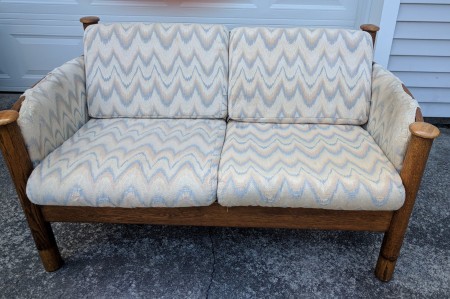 A wood frame love seat with light colored cushions.