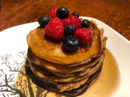 A stack of pancakes with syrup and fruit on the top.