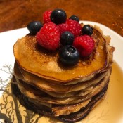 A stack of pancakes with syrup and fruit on the top.