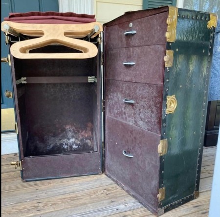 An open steamer chest with hangers and drawers.