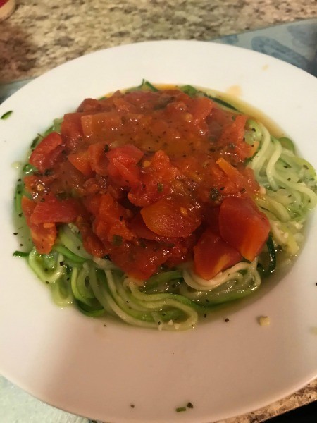Topping the zucchini spiral noodles with fresh tomato sauce.