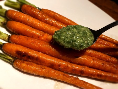 Spooning pesto on a plate of roasted carrots.