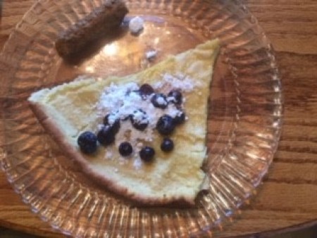 A plate containing a slice of Dutch Baby, with powdered sugar and blueberries on top.