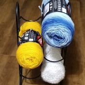 Three skeins of yarn in a wire wine rack.