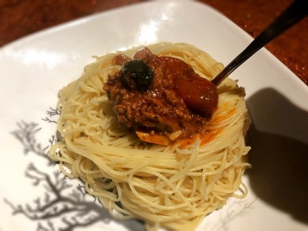 Spooning bolognese sauce on top of pasta.