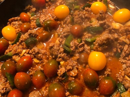 Adding whole cherry tomatoes to the ground beef mixture.