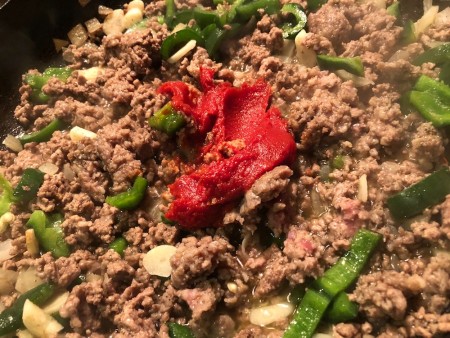 Adding tomato paste to the ground beef mixture.