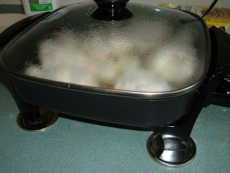 An electric frying pan with metal canning lids under the feet.