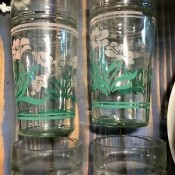 A set of glasses with white painted flowers and green leaves.