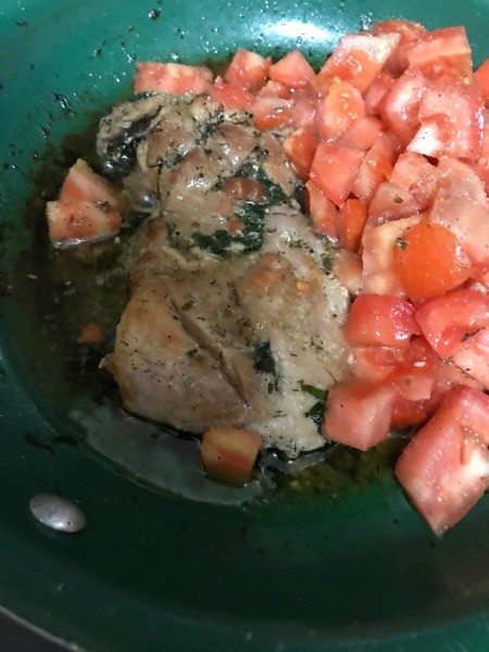 A pan of chicken with the tomato mixture being added.
