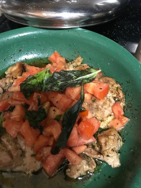 A pan with chicken, tomatoes and flavorings for Caprese chicken.