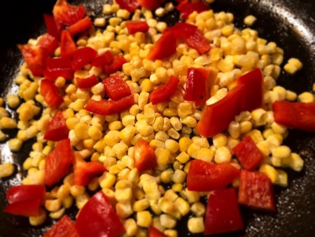 Corn and red peppers being sauteed in a pan.