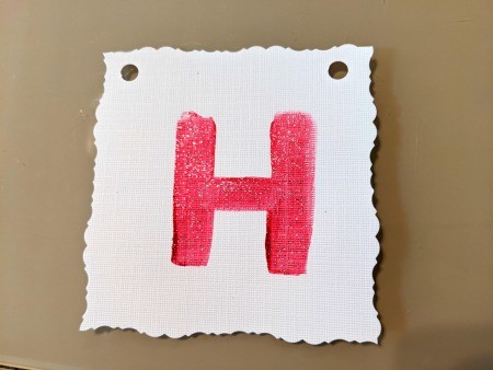 Painted Happy Birthday Banner - square with the letter H that has been cut with decorative scissors and had holes punched in the upper corners