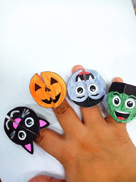 Paper Monster Rings - child's hand with a black cat, Jack 'o Lantern, vampire, and Frankenstein ring their fingers