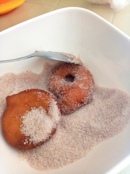 Rolling hot doughnuts in cinnamon sugar.