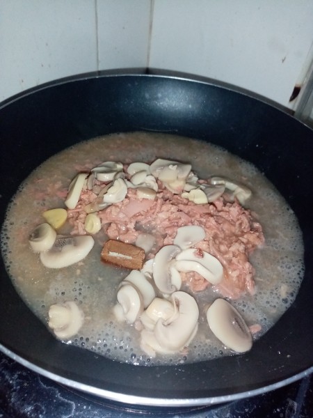 Adding tuna and mushrooms to a frying pan.