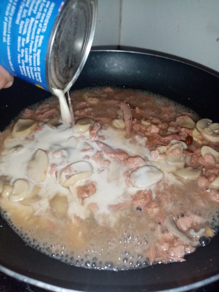 Adding a can of coconut milk to the pan.