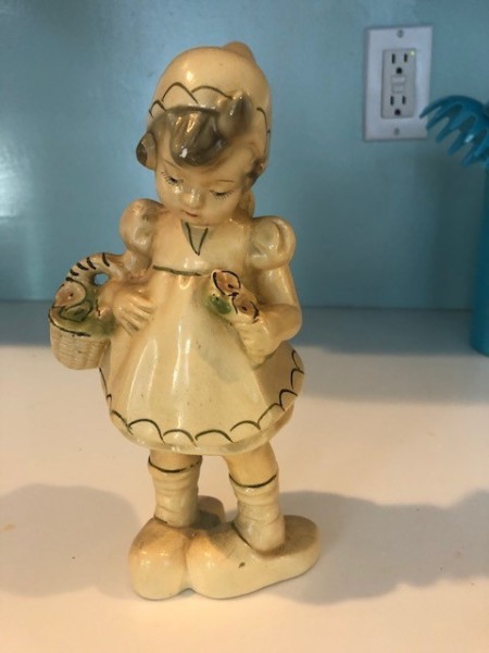 A ceramic figurine of a young girl with a basket.