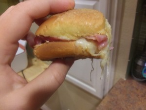 A person holding a ham and cheese slider.