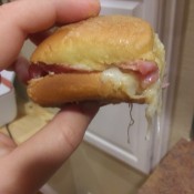 A person holding a ham and cheese slider.