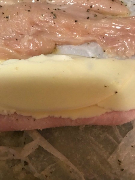 Stacking ham and cheese on top of the chicken breast.